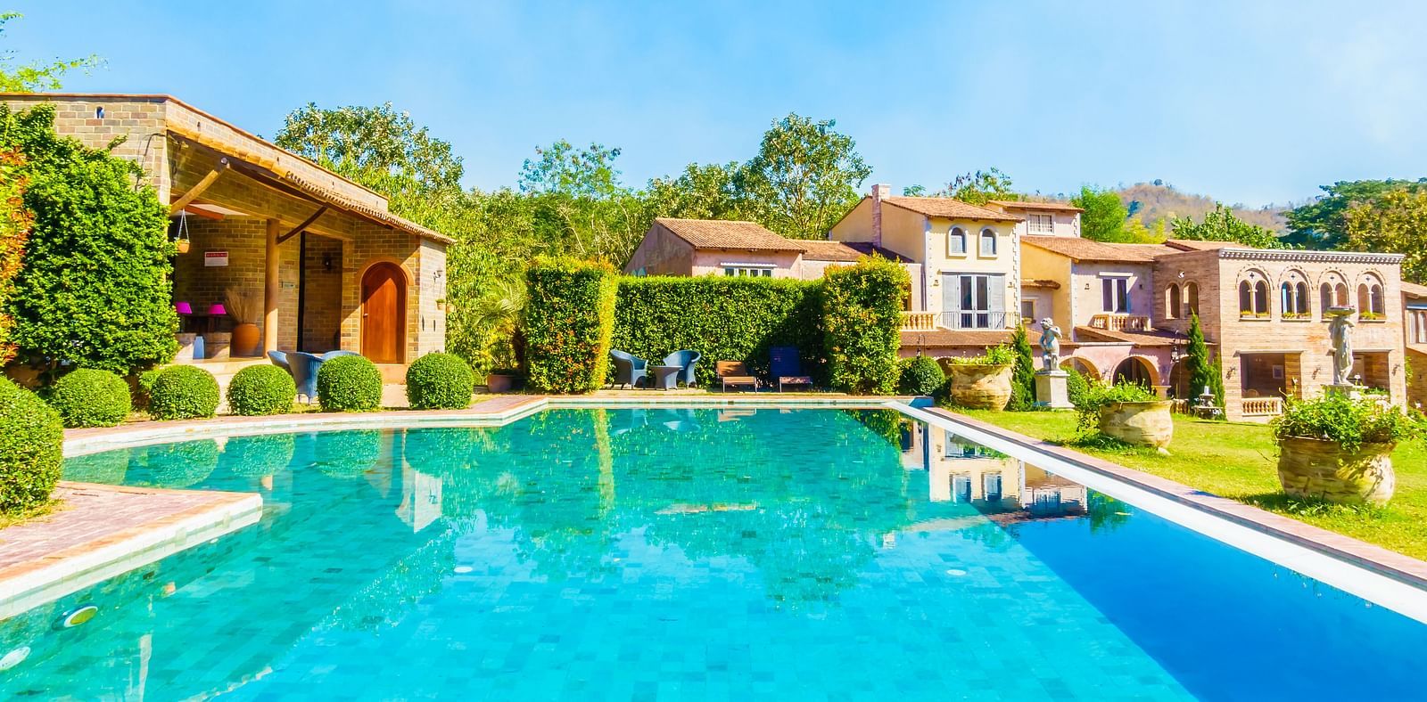 Swimming pool surrounded by the resort pathway, lined with well-trimmed bushes on both sides.