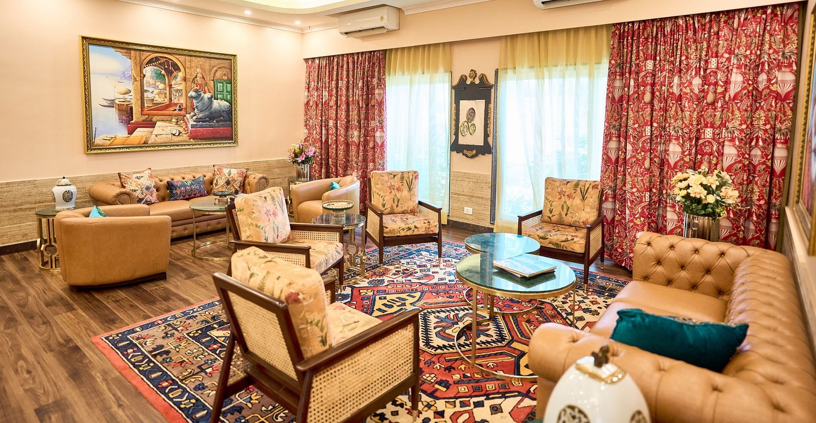  A seating area with plush furniture arranged around the table, curtains drawn to the side, and a wall-mounted painting at Mayfair Manor, Alibag