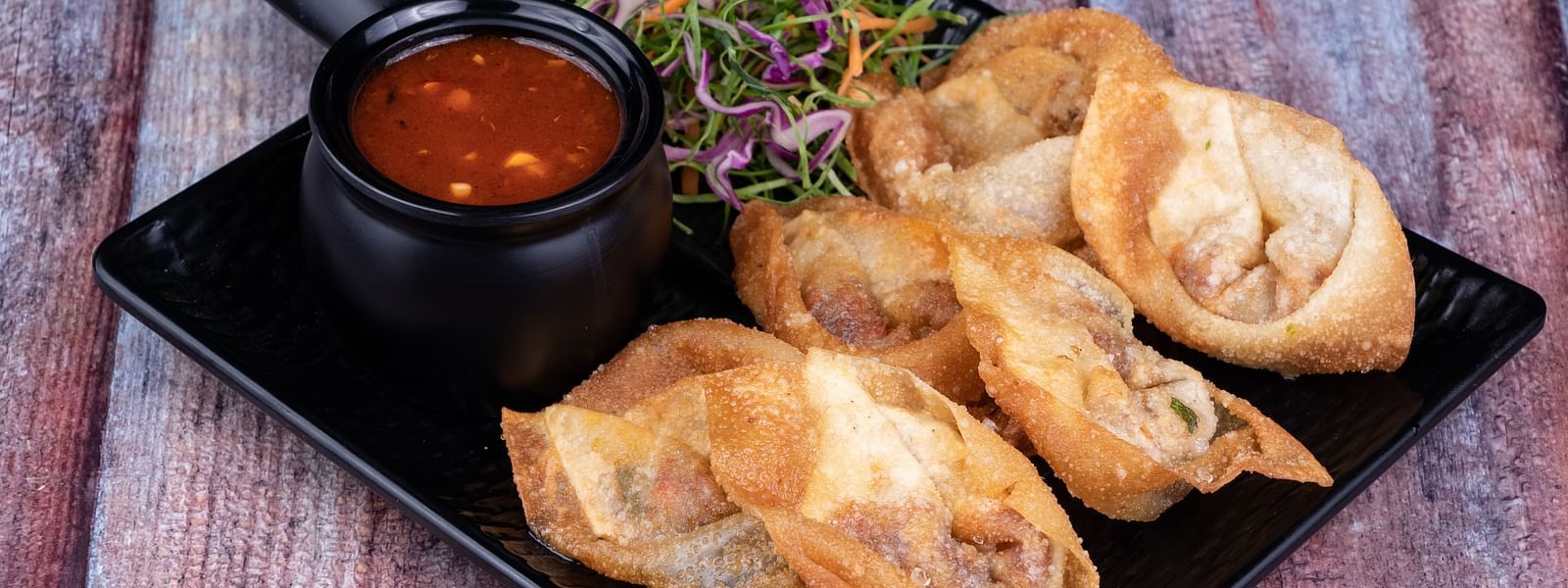 Golden-brown fried wontons on a black plate with a dip - The President Hotel, Kumara Park, Bangalore