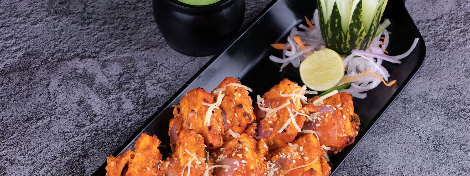 Spicy tandoori chicken served with mint chutney and onion salad on a black platter. - The President Hotel, Kumara Park, Bangalore