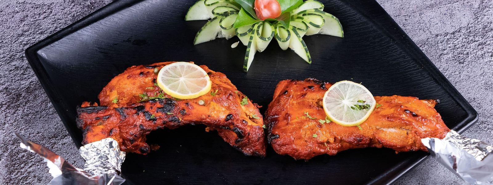 Grilled chicken drumsticks with foil-wrapped ends, presented on a black plate with a garnish - The President Hotel, Kumara Park, Bangalore