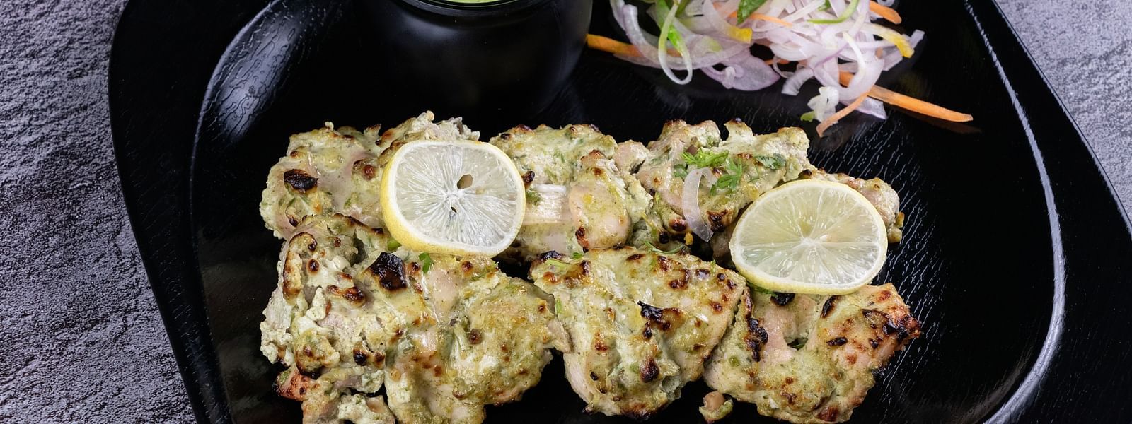 An image of tandoori malai chicken presented with lemon wedges and a side salad on a black dish - The President Hotel, Kumara Park, Bangalore