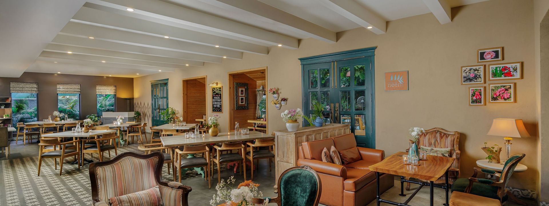 Dining area at Karma Chalets with multiple tables, chairs, white ceiling beams, and wall art in a well-lit room.