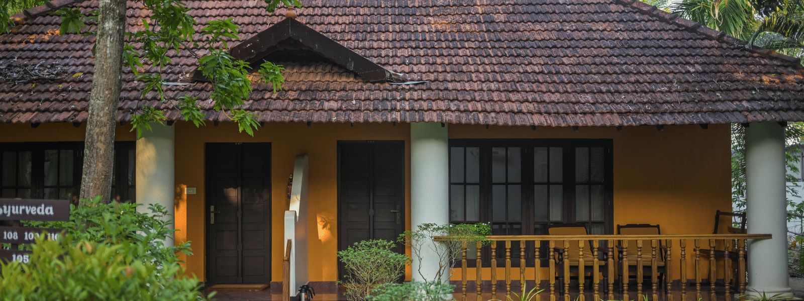 A traditional guest villa at Ayur On The Beach Nattika featuring a tiled roof, large pillars, and a wooden verandah.