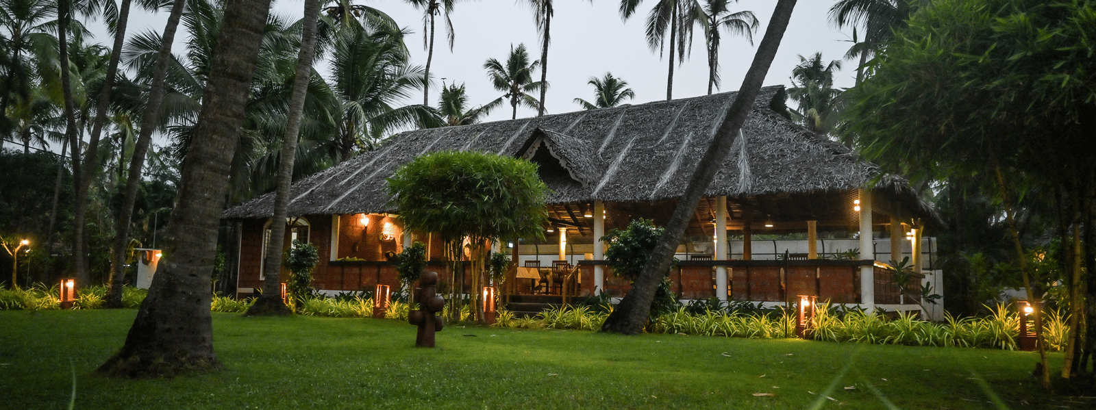 The lush green grounds of Ayur On The Beach Nattika with a traditional villa in the background.