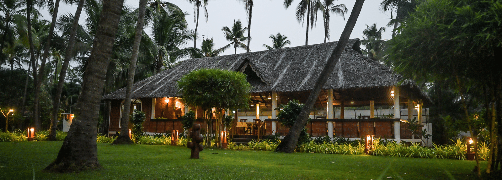 The lush green grounds of Ayur On The Beach Nattika with a traditional villa in the background.