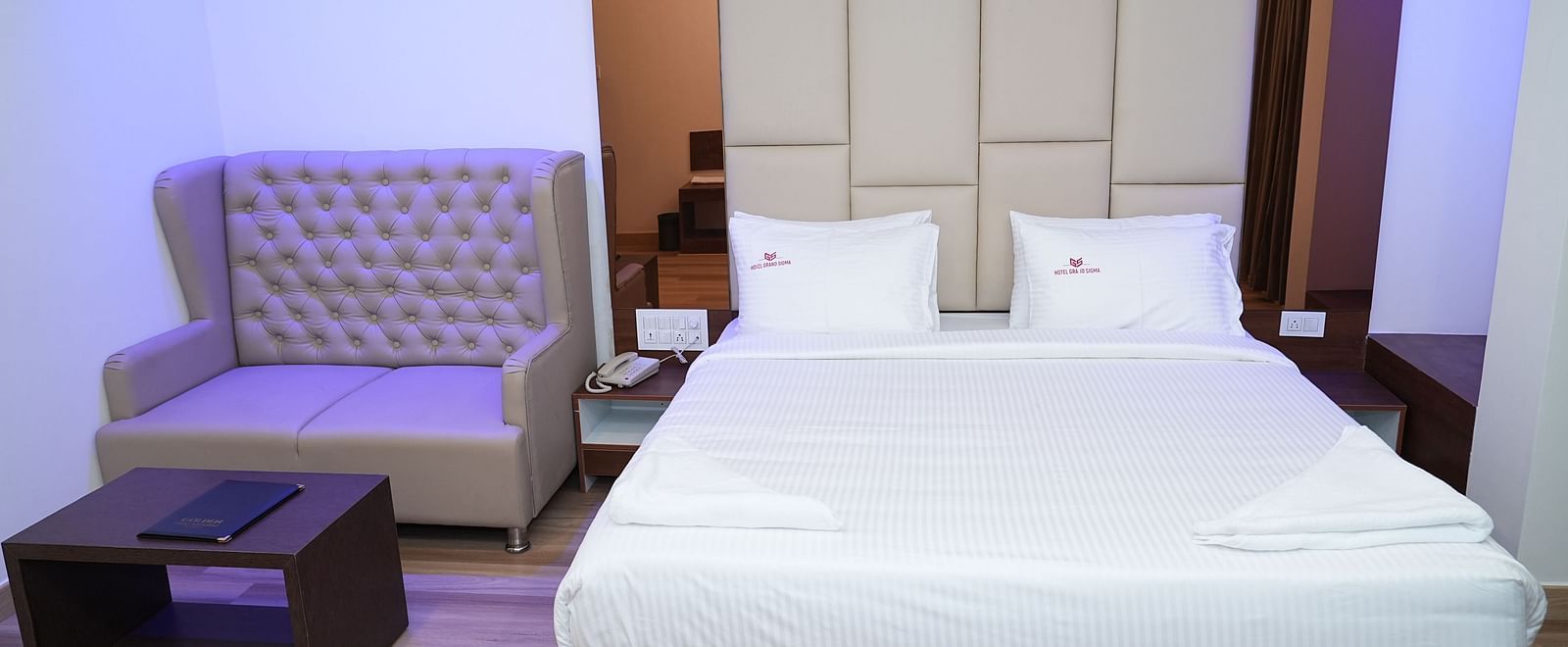 a double bed along with a beige coloured couch with a coffee table in front of it - Hotel Grand Sigma