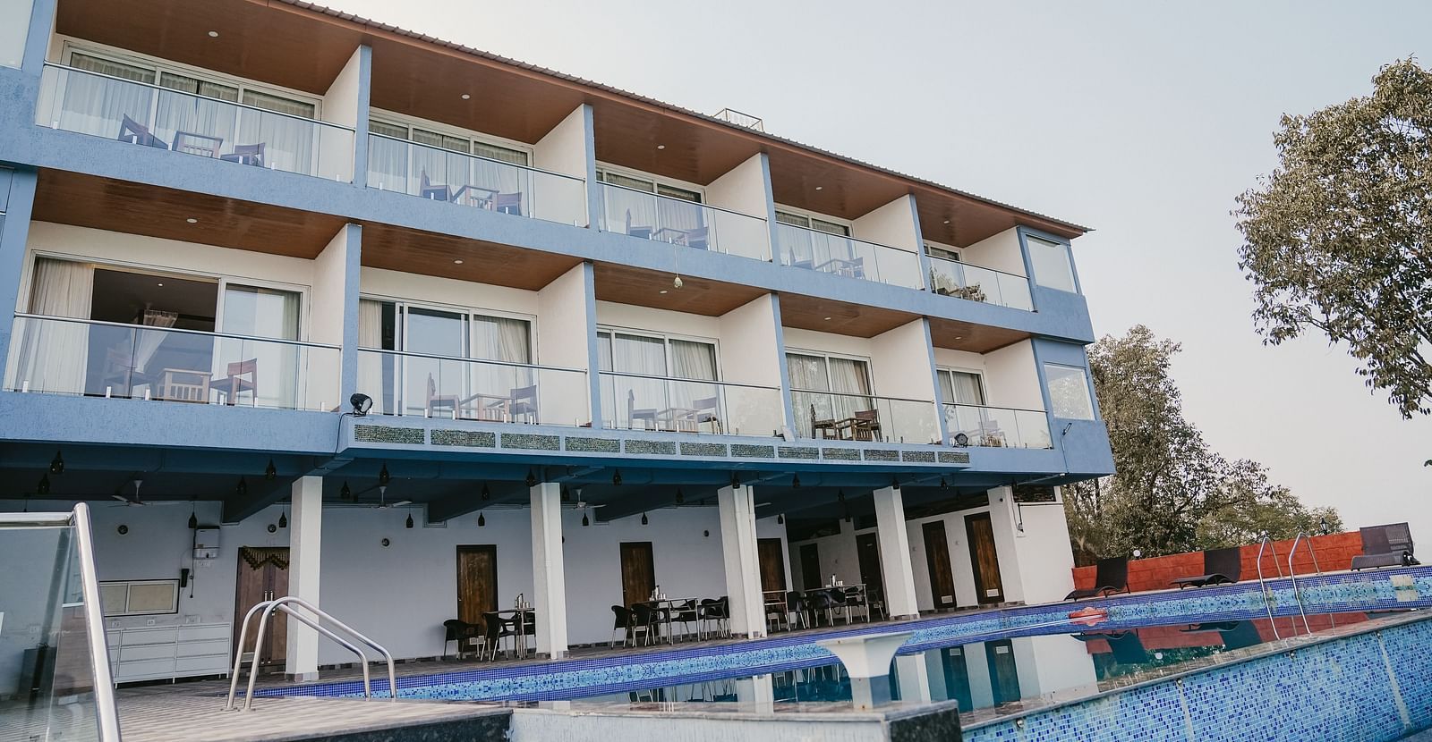 A facade image of the Nisarga Lake Resort with the swimming pool in the front surrounded by greenery