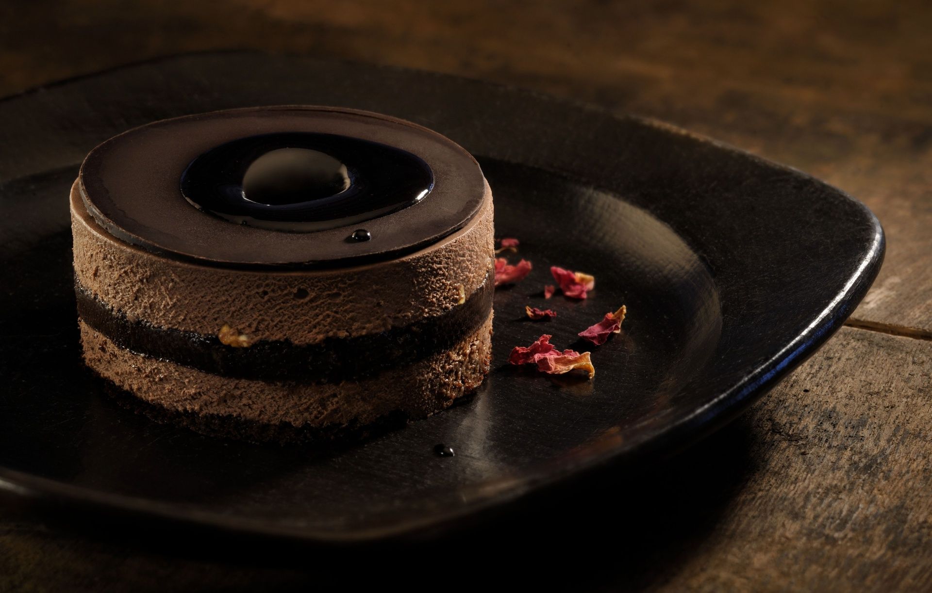 Dark chocolate mousse cake with a glossy top and petals.