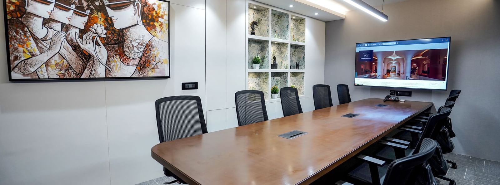 The boardroom at M2 Square by Monday Premium featuring a long wooden table along with an abstract painting hung on the wall.