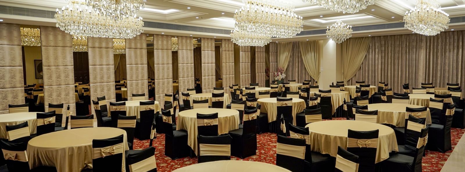 Corner view shot of the ballroom at M2 Square by Monday Premium featuring various tables surrounded by black coloured chairs.