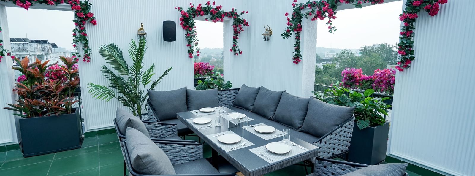 A wide angle shot of a dining table with a capacity of 6 people featuring a white coloured wall behind it at the Sky Roof during the day at M2 Square by Monday Premium.