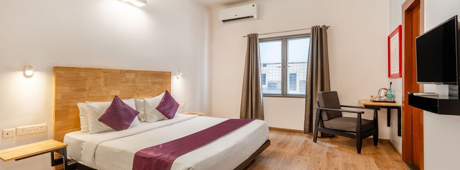 A spacious hotel room with a bed, wooden flooring, a chair and a wall mounted tv - Monday Hotels HITEC City, Hyderabad