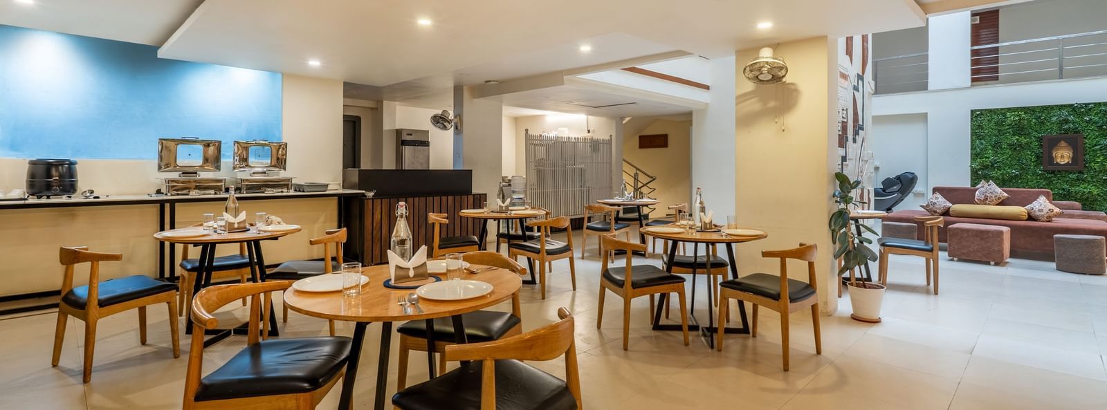 A large dining space with wooden tables, chairs, and an open kitchen view - Monday Hotels HITEC City, Hyderabad
