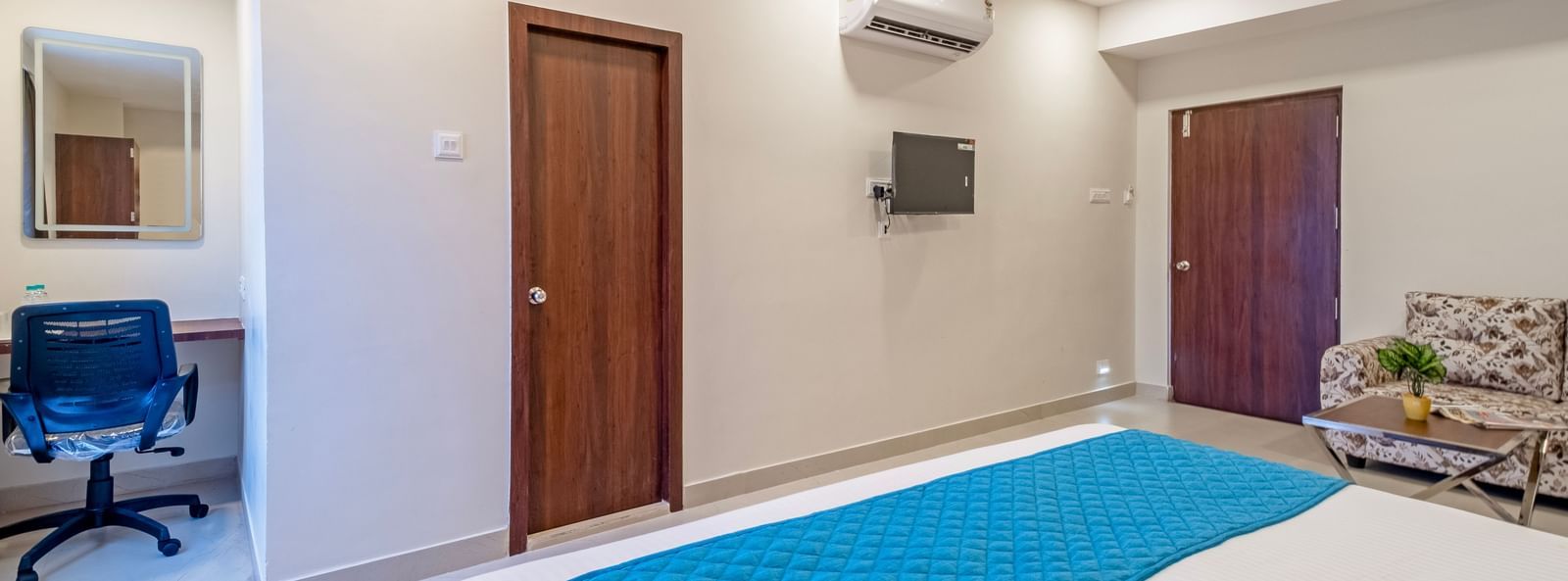 Room view with double bed blue runner wardrobe work desk television and air-conditioning at Swarna's The Capital.