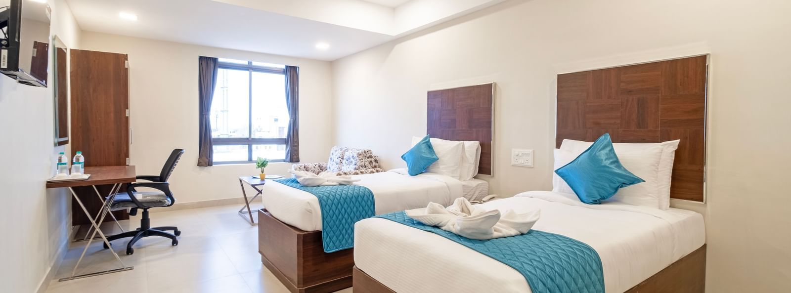 Twin beds with fresh linens blue runners seating area and bright ambience creating comfort at Swarna's The Capital.