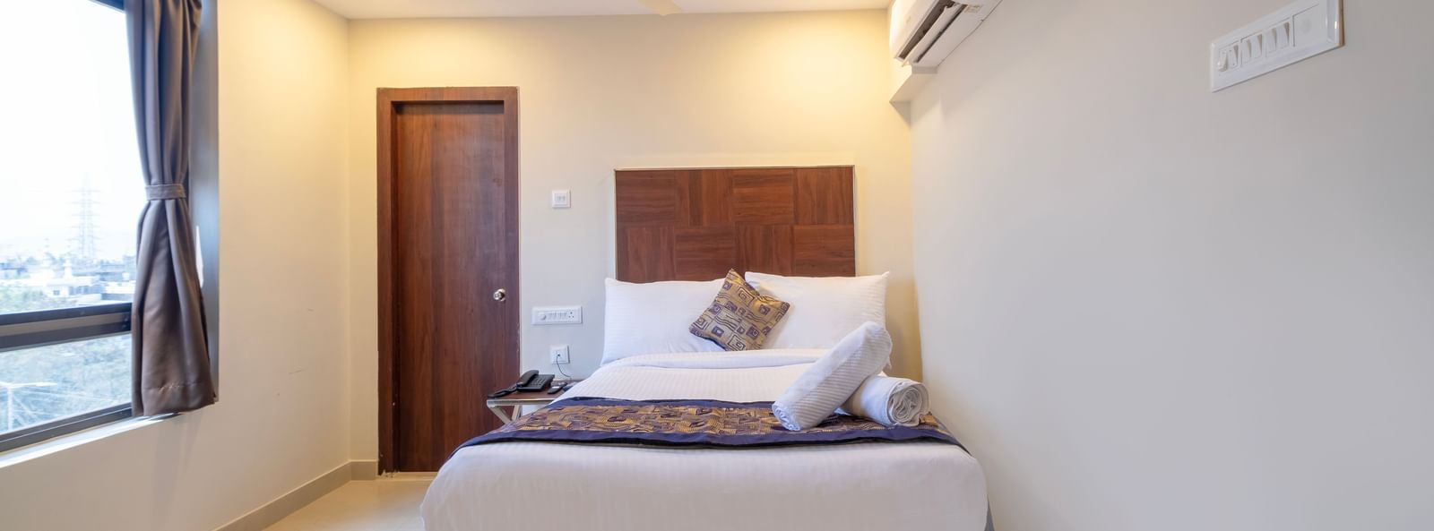 Bright bedroom with double bed soft furnishings ceiling fan air-conditioning and window for natural light at Swarna's The Capital.