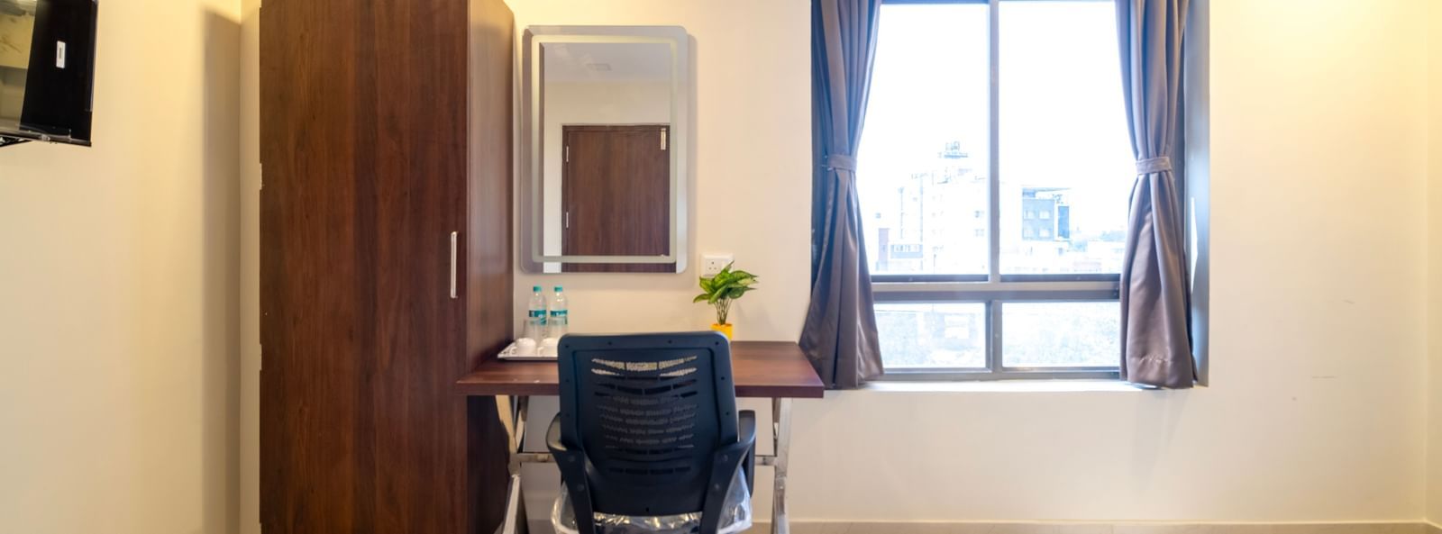 Work desk with ergonomic chair wardrobe mirror and window providing a functional and airy workspace at Swarna's The Capital.