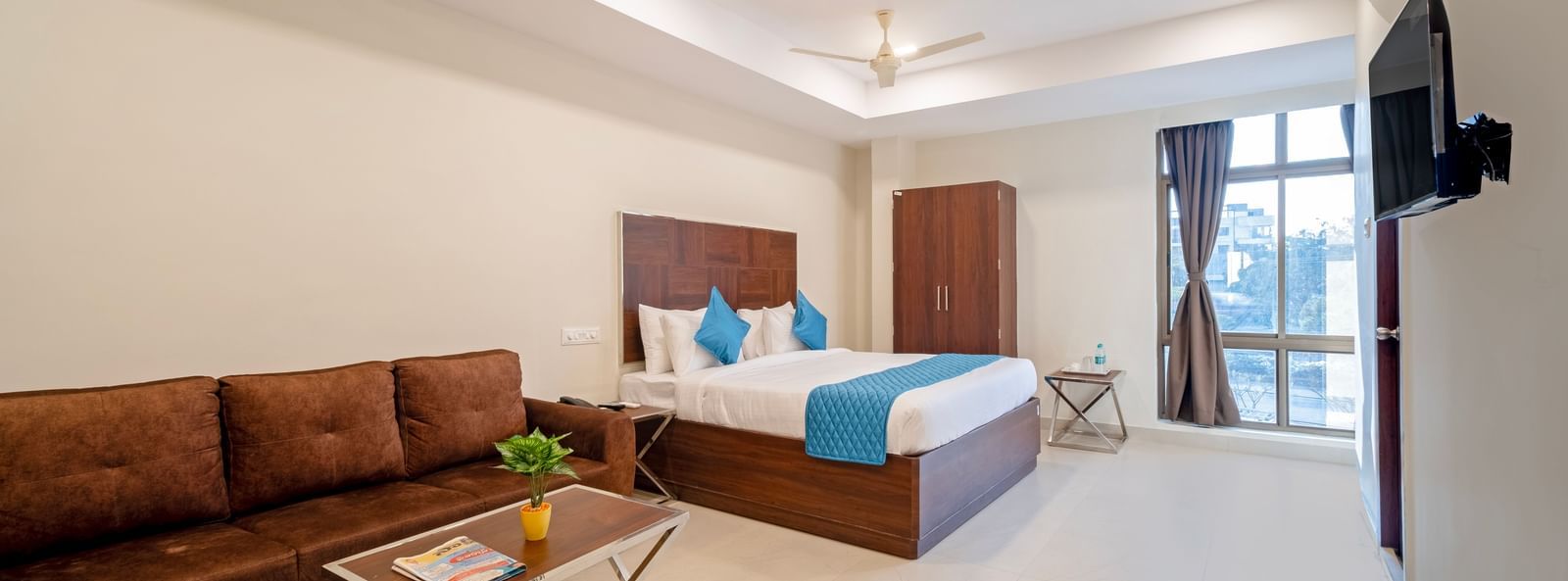 Bedroom with double bed blue decor sofa seating area television and soft lighting for a homely stay at Swarna's The Capital.