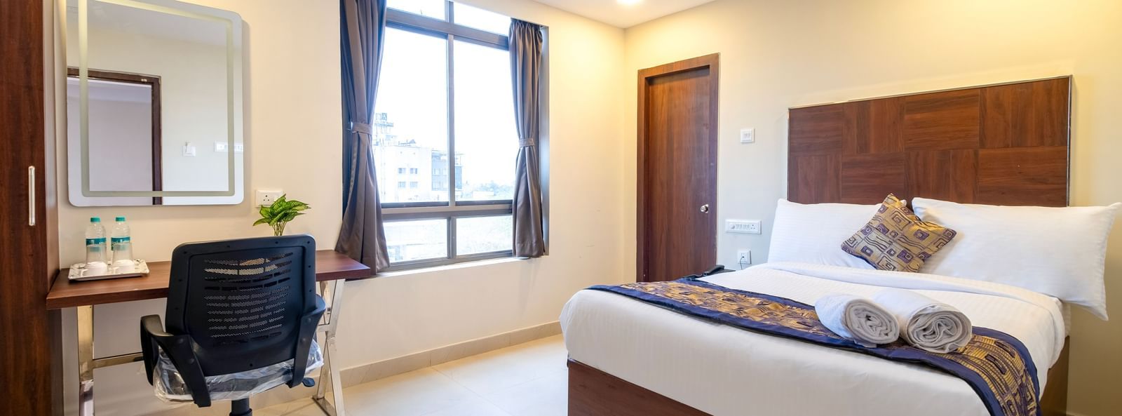 Comfortable bedroom with double bed work desk mirror chair and large window offering natural light at Swarna's The Capital.