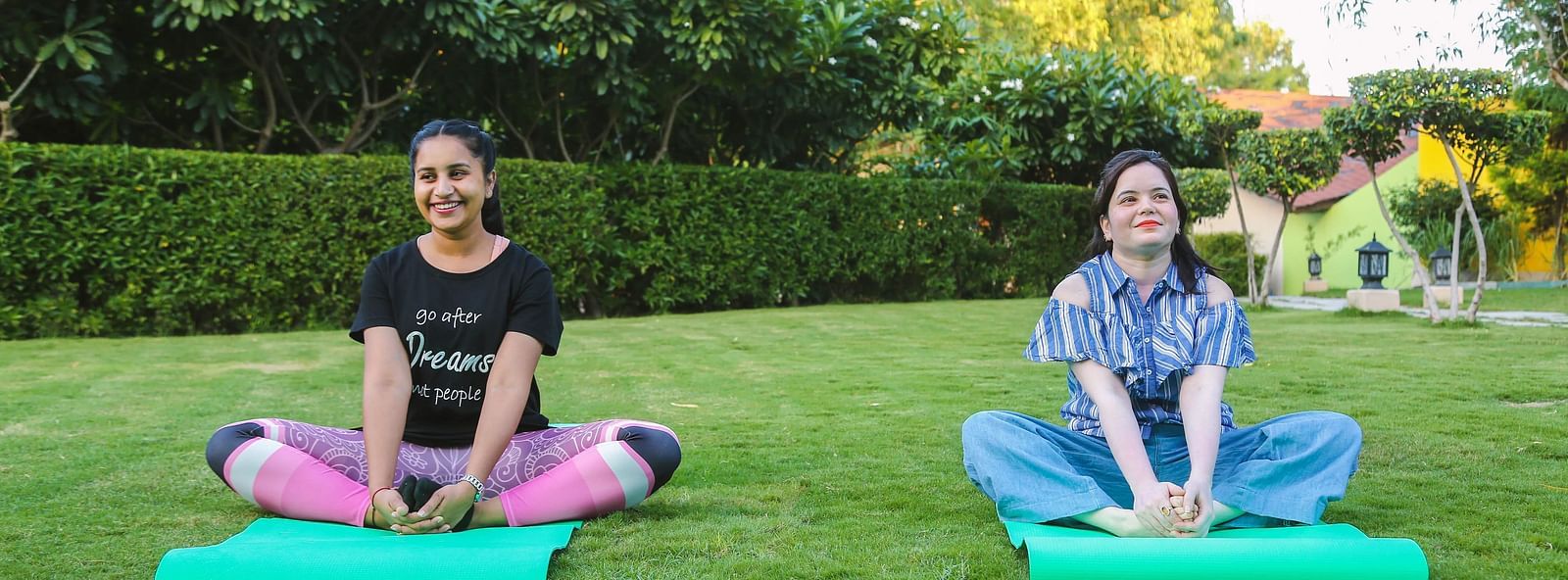 Two women meditating on yoga mats in a green garden.