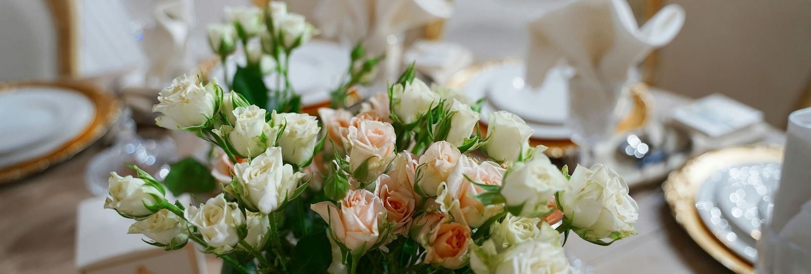 A close up shot of a beautiful flower vase with a lot of white and pink roses on a dining table.