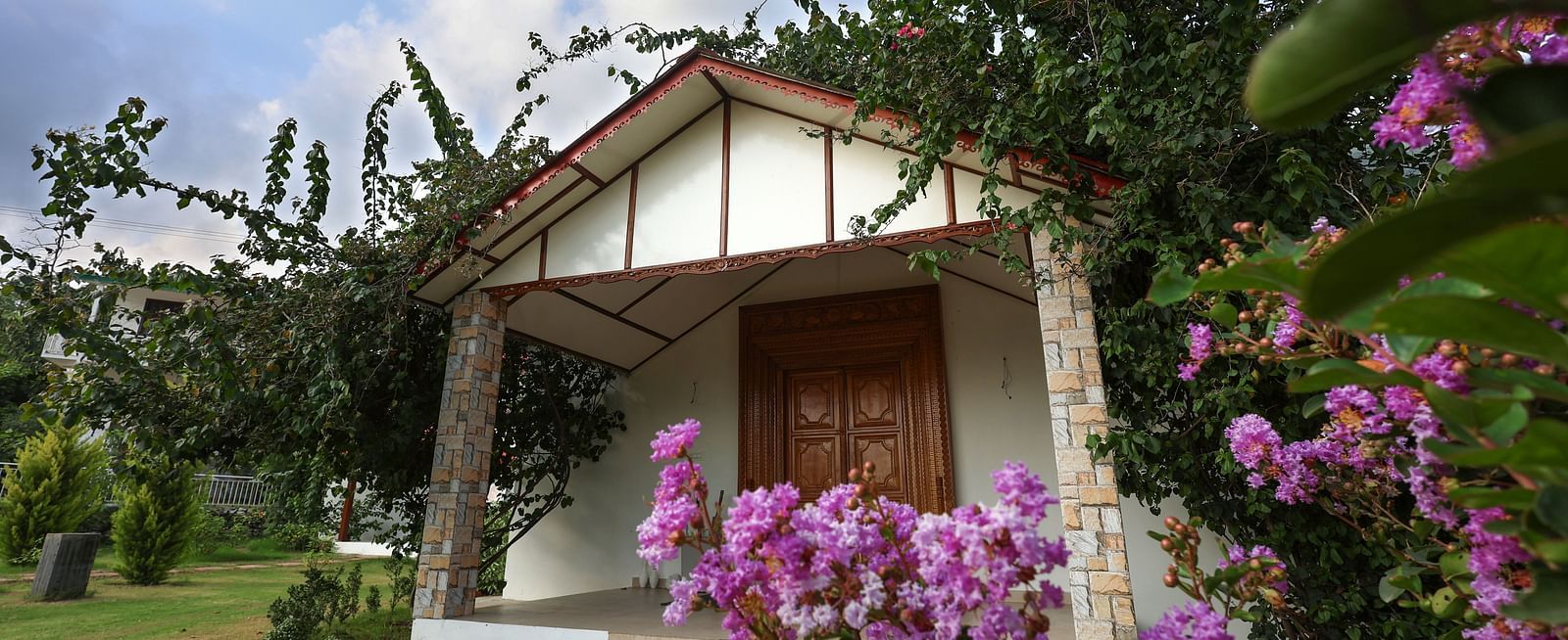 A charming cottage entrance with stone pillars and blooming purple flowers - Neer Ganga Resorts