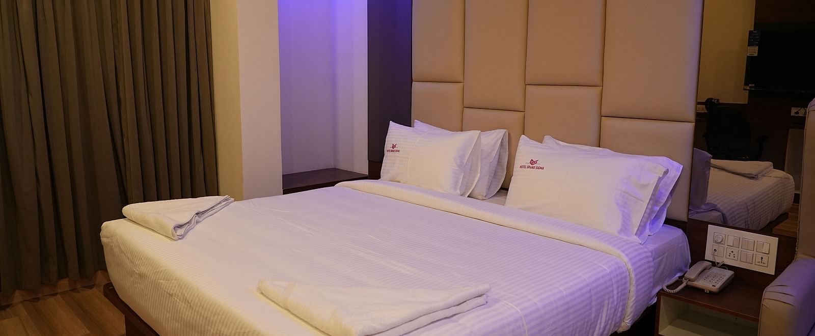 corner view of the double bed of the suite with cushioned headboard behind the bed and close curtains in the corner of the room - Hotel Grand Sigma