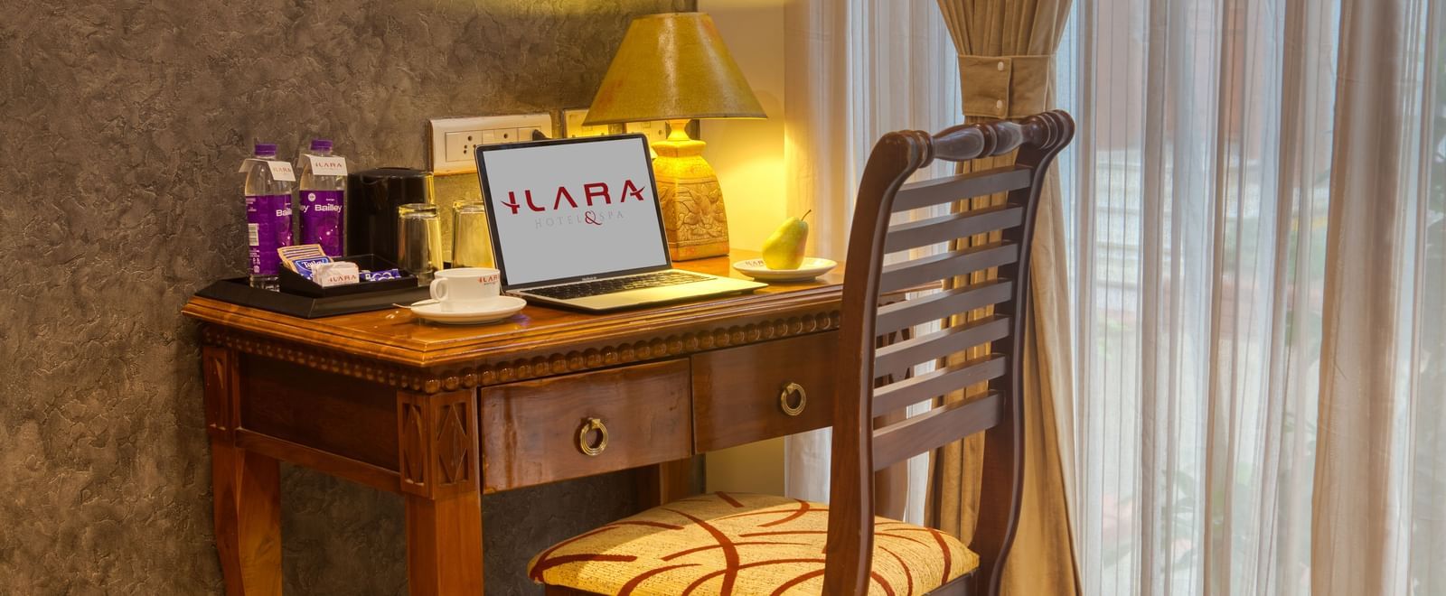 Dedicated wooden work desk with welcome kit and tea setup near a sheer curtain at Ilara Hotels & Spa, OMR, Chennai