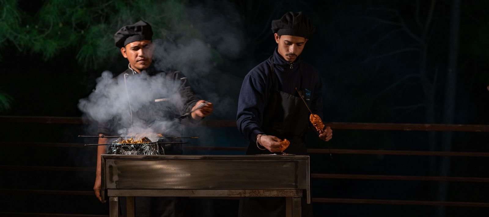 Two chefs preparing barbecues with smoke rising from the sizzling grills at BluSalzz Escapade Resort, Lansdowne