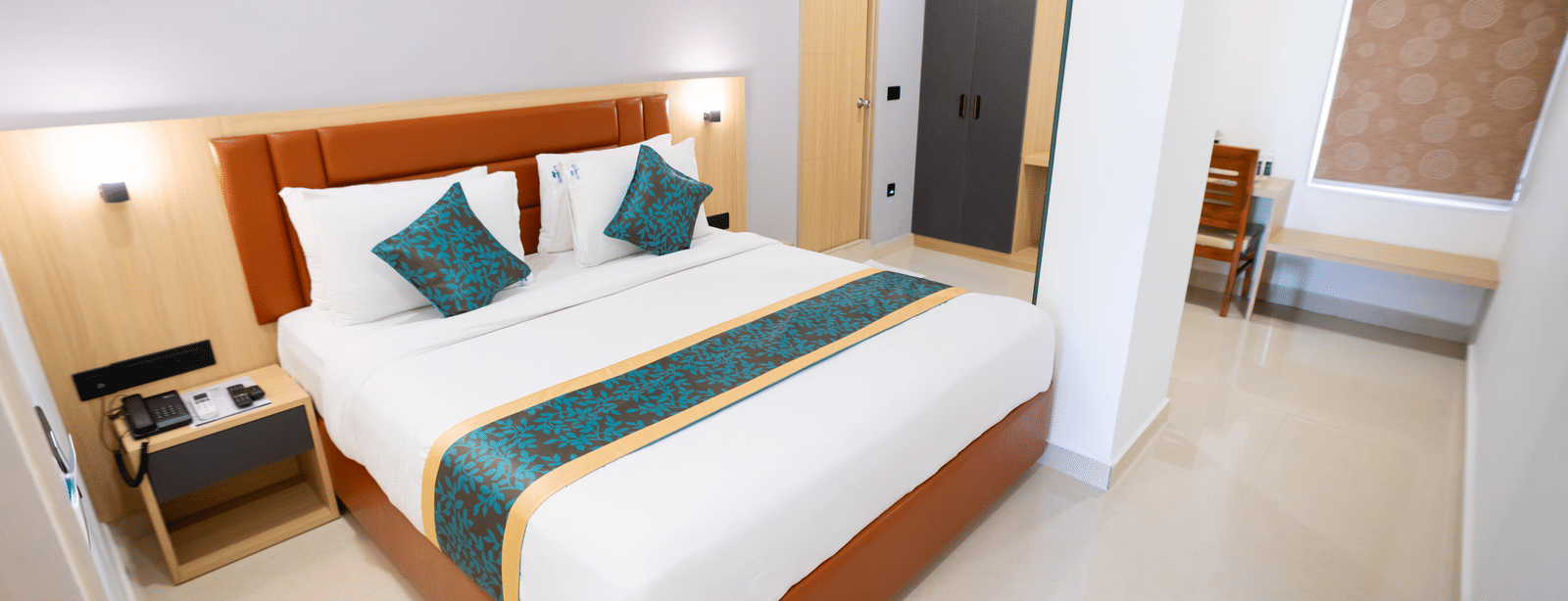 A spacious room with a large bed, a bedside table, and a doorway to the side at Sunrise Business Hotel, Hyderabad.