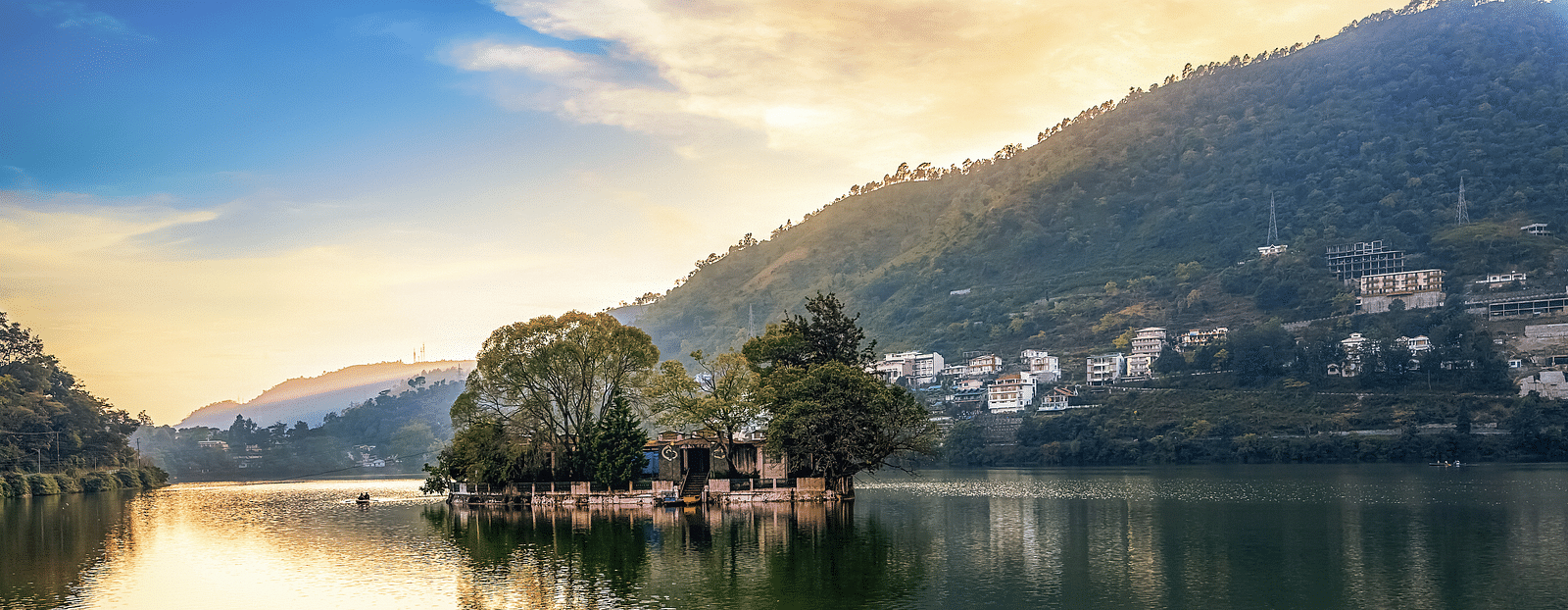 A wide-angle view of Bhimtal Lake with a serene mountain backdrop and ducks peacefully swimming in the calm waters.
