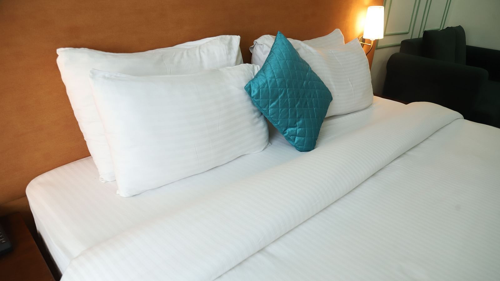 A close-up of a bed with white linens, several white pillows, and a single teal cushion - Asian Suites IFFCO Metro, Gurgaon