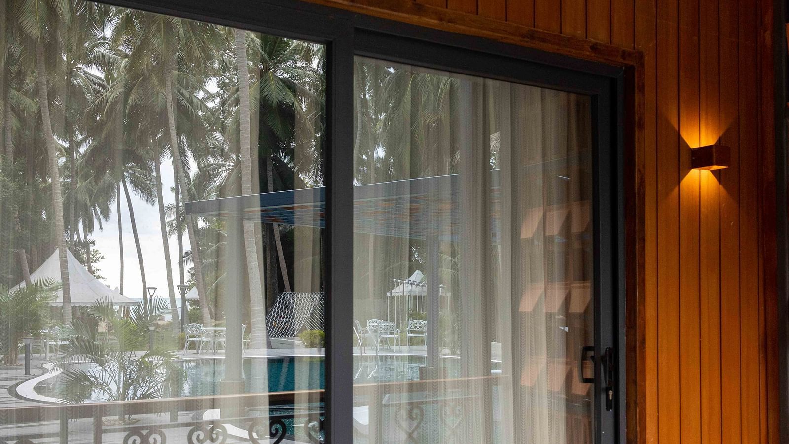 Coral Sapphire at Coral Reef Resort and Spa in Havelock displaying a shot of the glass door to the balcony with the swimming pool and trees reflecting on the glass