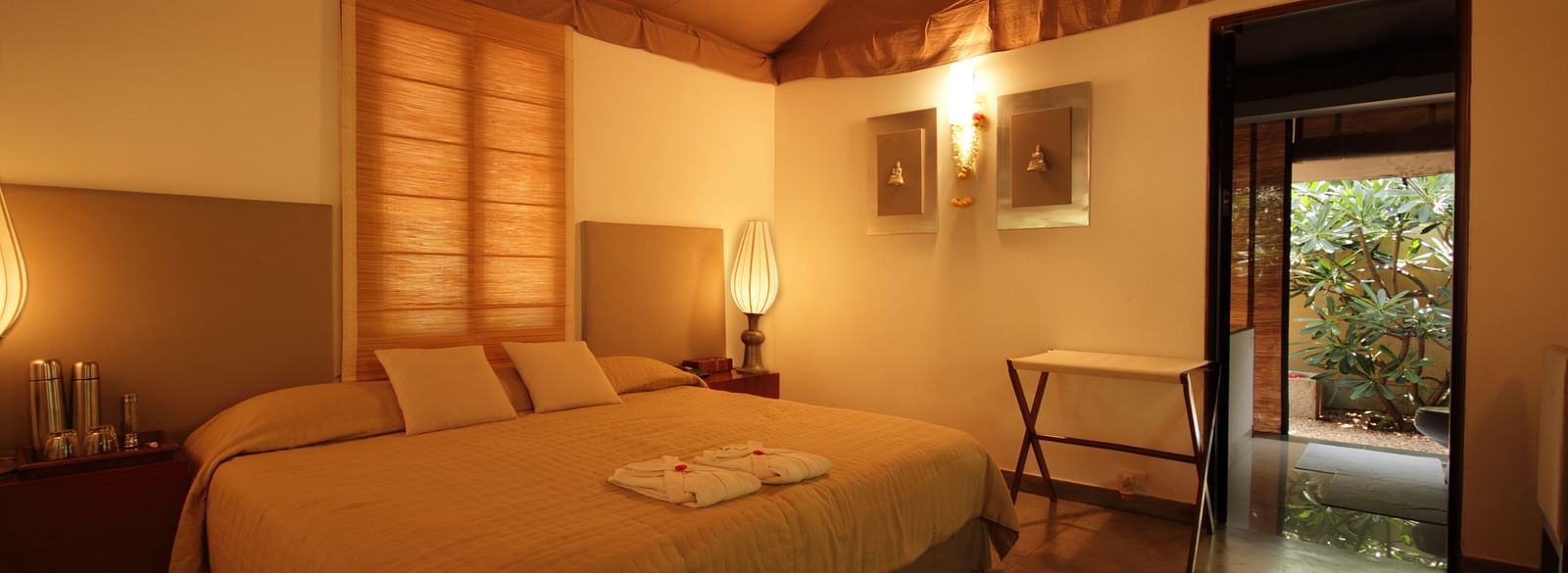 A bedroom with a bed, lamps, and a view of a garden - Shreyas Retreat