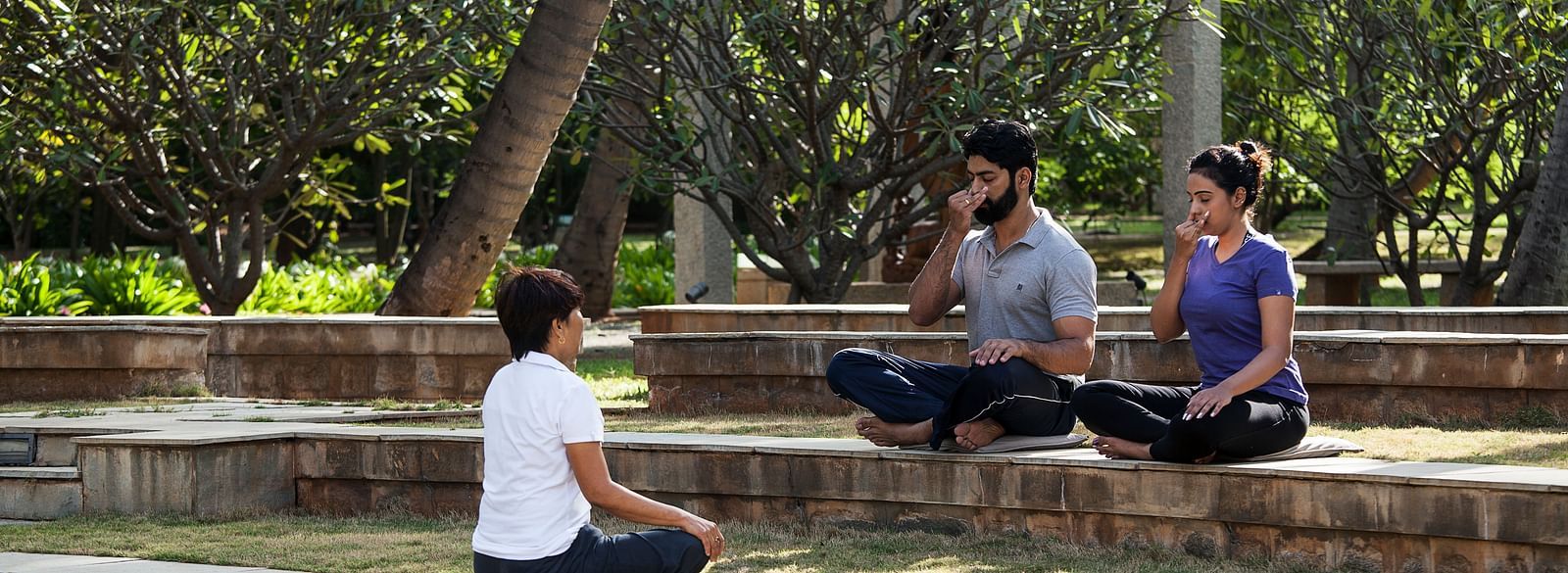 People sitting on steps outdoors, trees, performing yoga - Shreyas Retreat