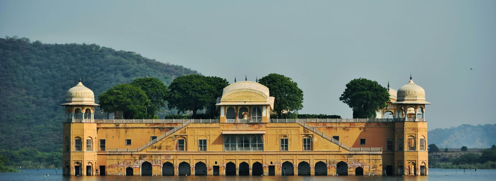 A palace partially submerged in the middle of a lake, with mountains and a misty sky in the background.