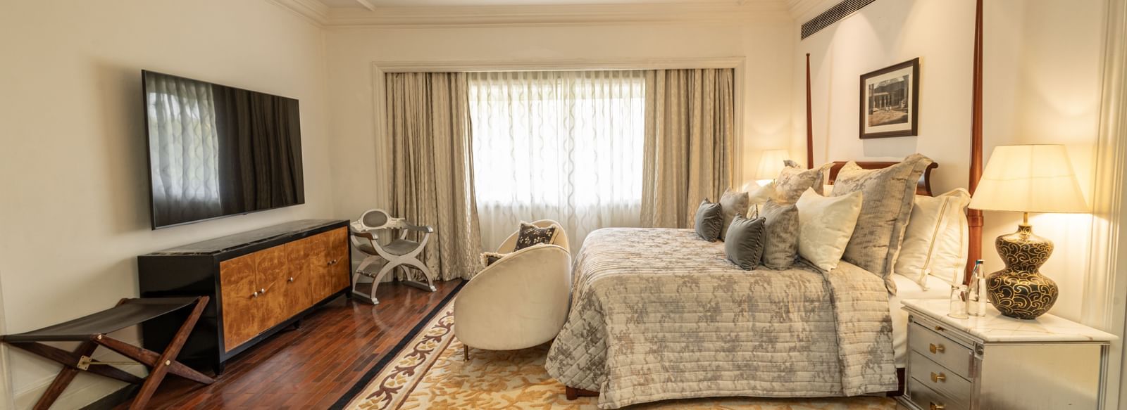 The Claridges New Delhi bright bedroom is furnished with two double beds, dark wood floors, and a patterned rug.