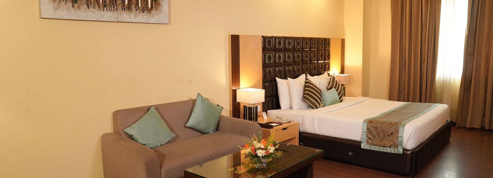 Spacious hotel room with a bed, seating area, and large window - Grand Plaza Lords Inn Jammu