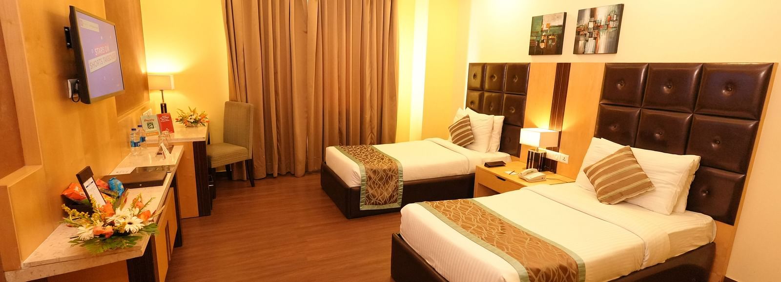 Hotel room with a bed featuring striped bedding and a television on the wall - Grand Plaza Lords Inn Jammu
