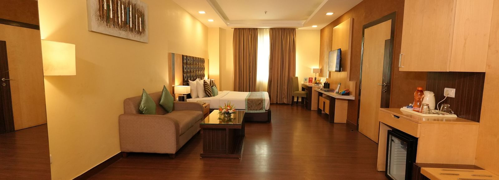 Hotel suite hallway leading to a seating area and a bed with striped bedding - Grand Plaza Lords Inn Jammu