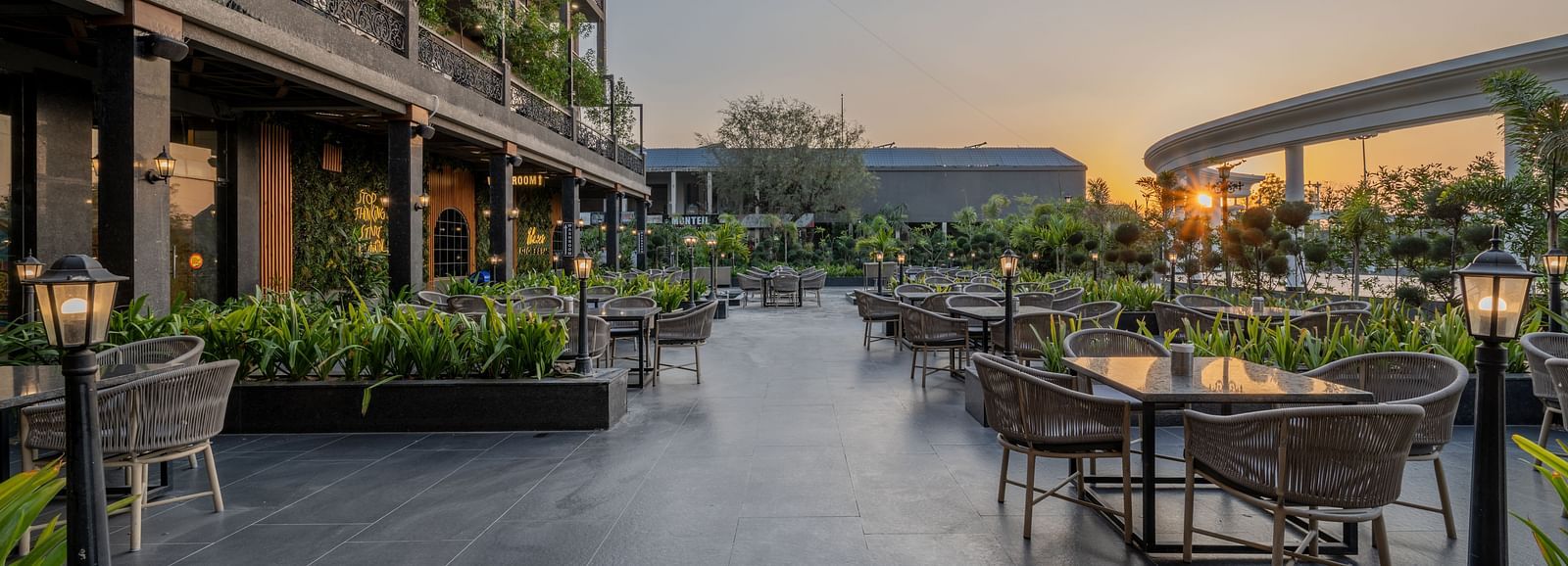 Outdoor seating area at Hotel Highway King, Bagru, with tables, chairs, greenery, and the hotel building in the background.