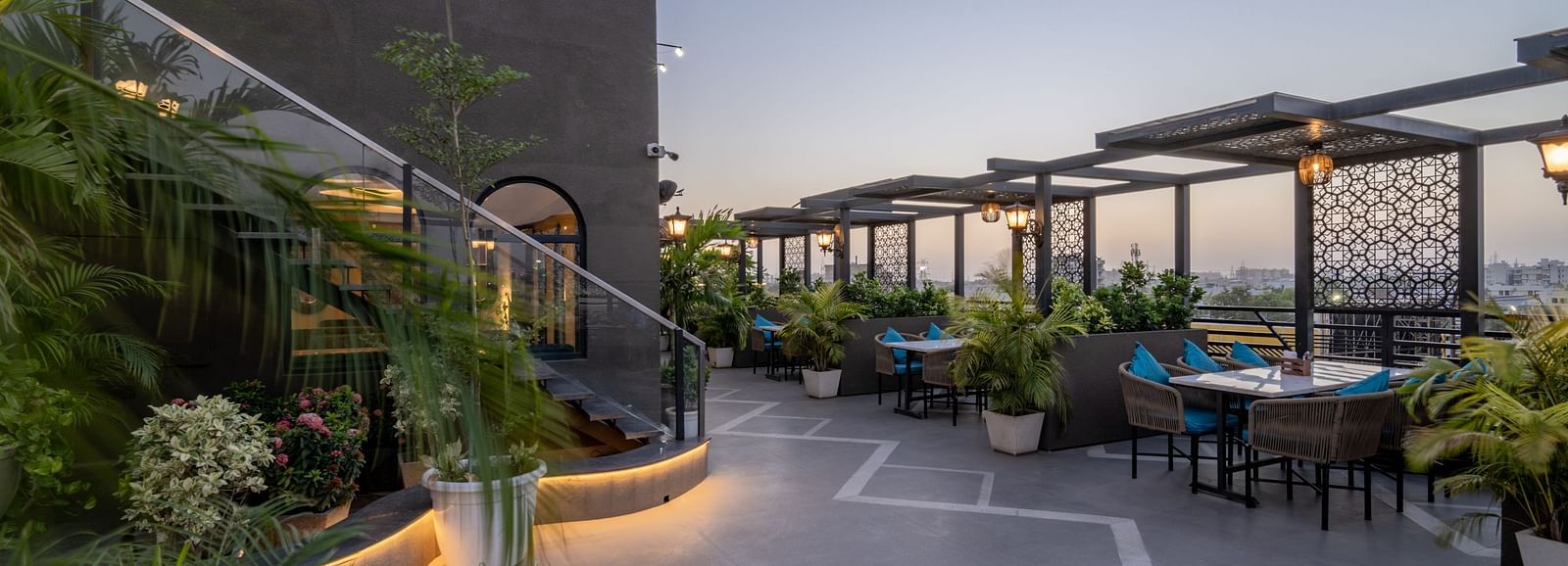 Evening rooftop walkway with potted plants, wall lamps, and covered seating at Hotel Highway King, Jaipur.
