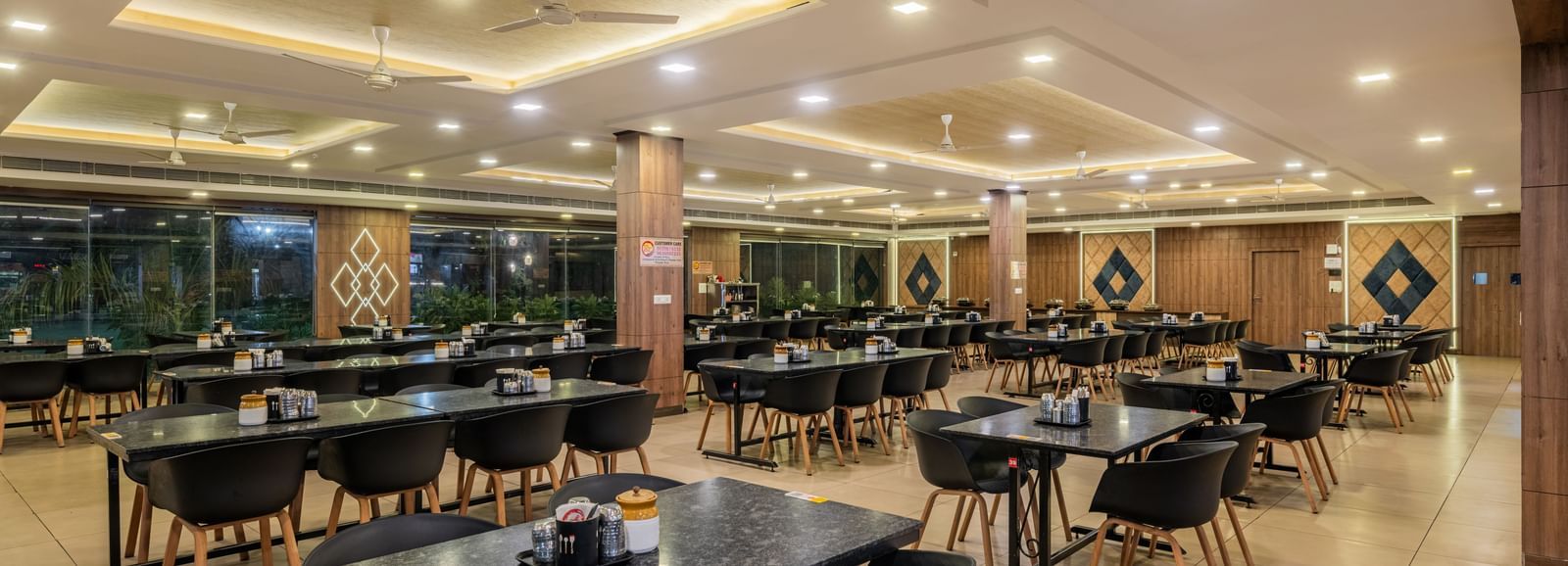 An empty, well-lit dining area inside the Hotel Highway King Shahpura, set with numerous tables and chairs.