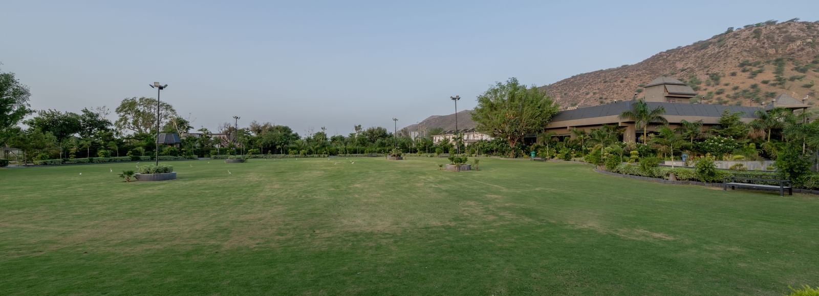 A large, well-maintained green lawn with distant hills at Hotel Highway King Shahpura.