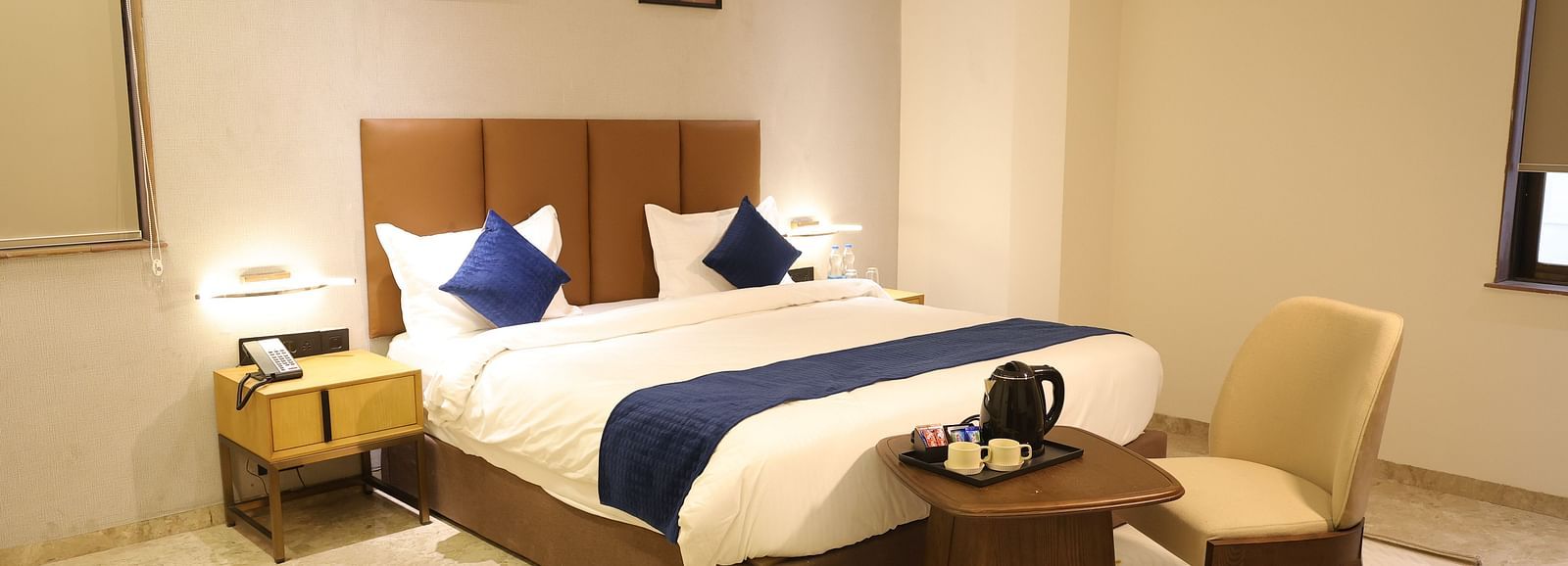 A spacious Deluxe Room at Lords Eco inn Jamnagar Maheshwari Nagar with a large bed two bedside tables and modern artwork.