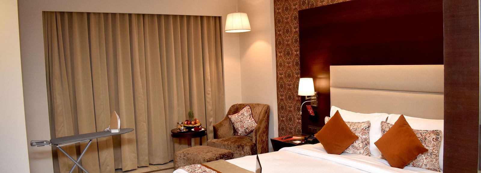 A hotel room features a bed with a laptop and bedside lighting at Lords Plaza Surat.