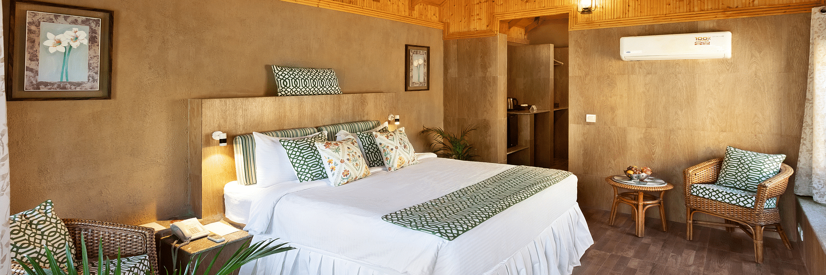 An image of an attic style bedroom featuring double size bed, a bedside table, flower pots, and a seating area at Suryavilas Luxury Resort & Spa, Kasauli