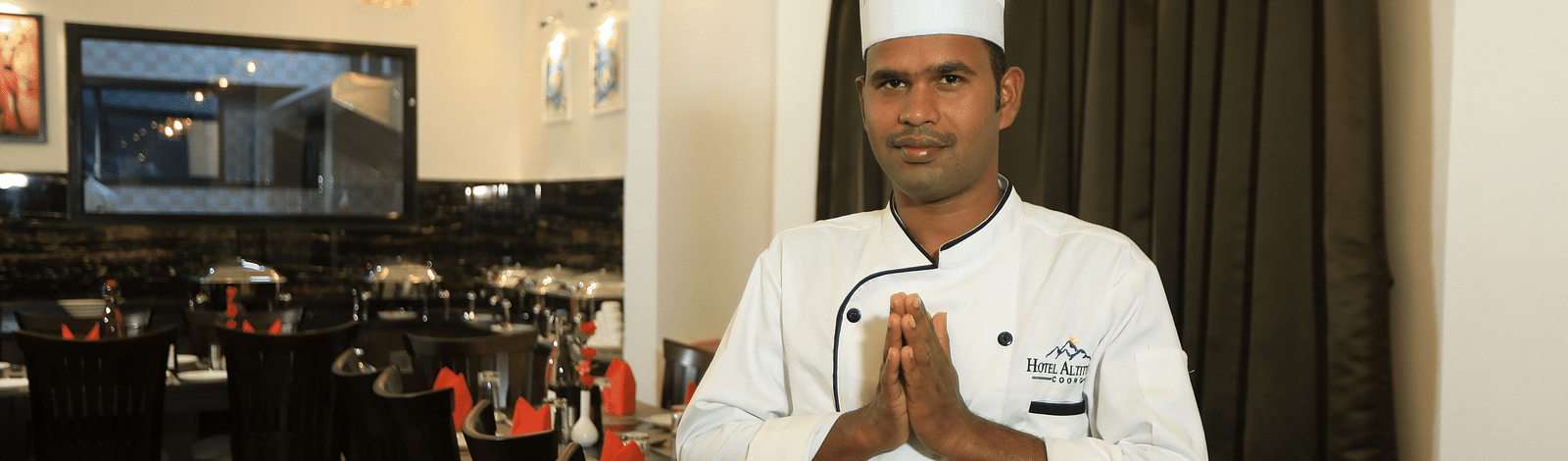 A man posing for a photograph with tables and chairs in the background at Hotel Altitude, Madikeri.