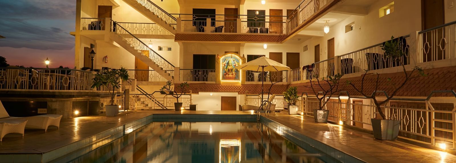 A nighttime view of Hotel Mamallaa Heritage, showcasing its illuminated facade and a beautifully lit swimming pool reflecting the lights.